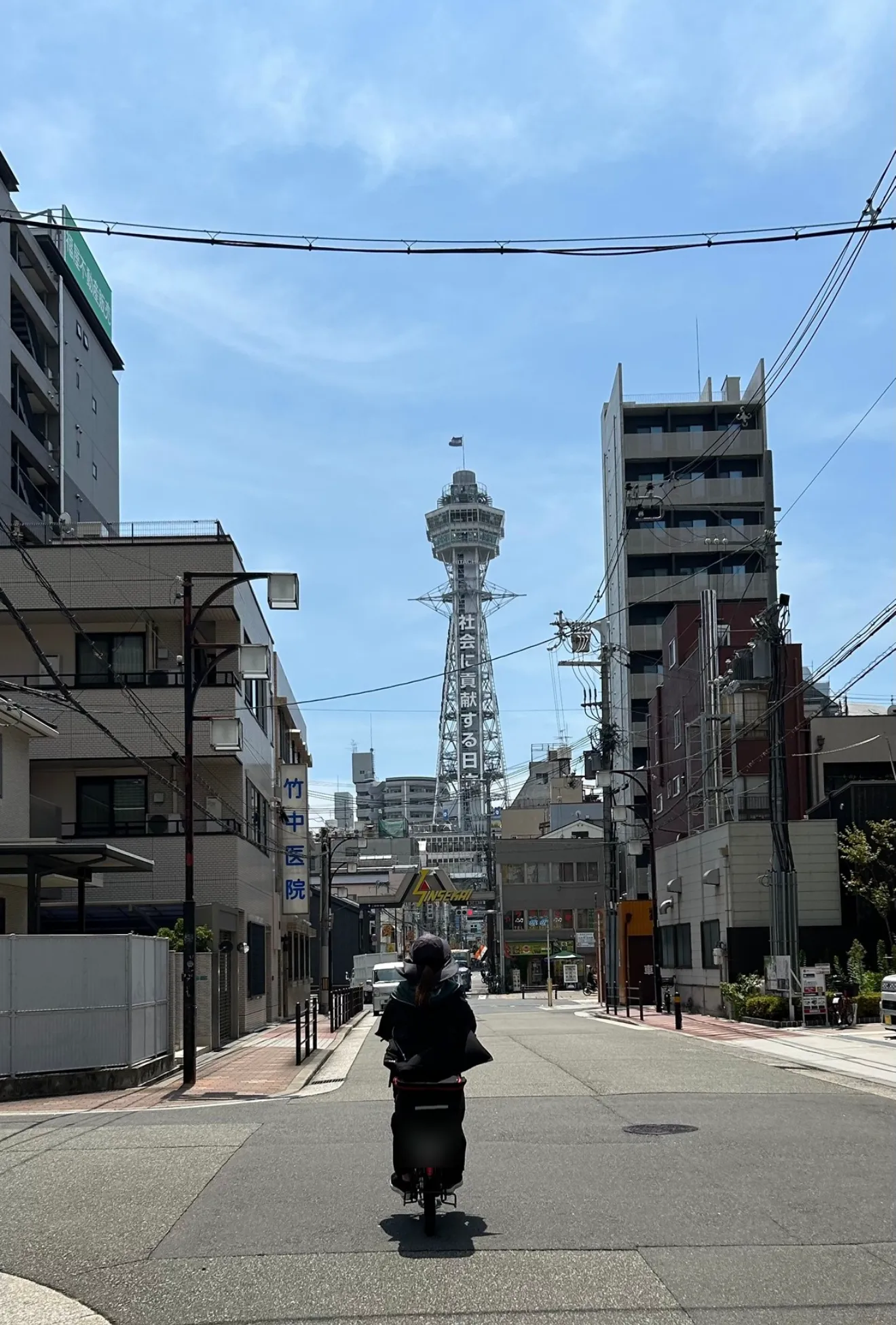 通天閣の見える町を、電動自転車で訪問に向かう看護師の後ろ姿